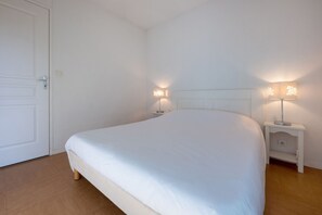 A neatly made bed in a room with white walls and a wooden floor. There are two bedside tables with lamps. - Le Domaine de L'océan (Saint-Brevin-les-Pins)