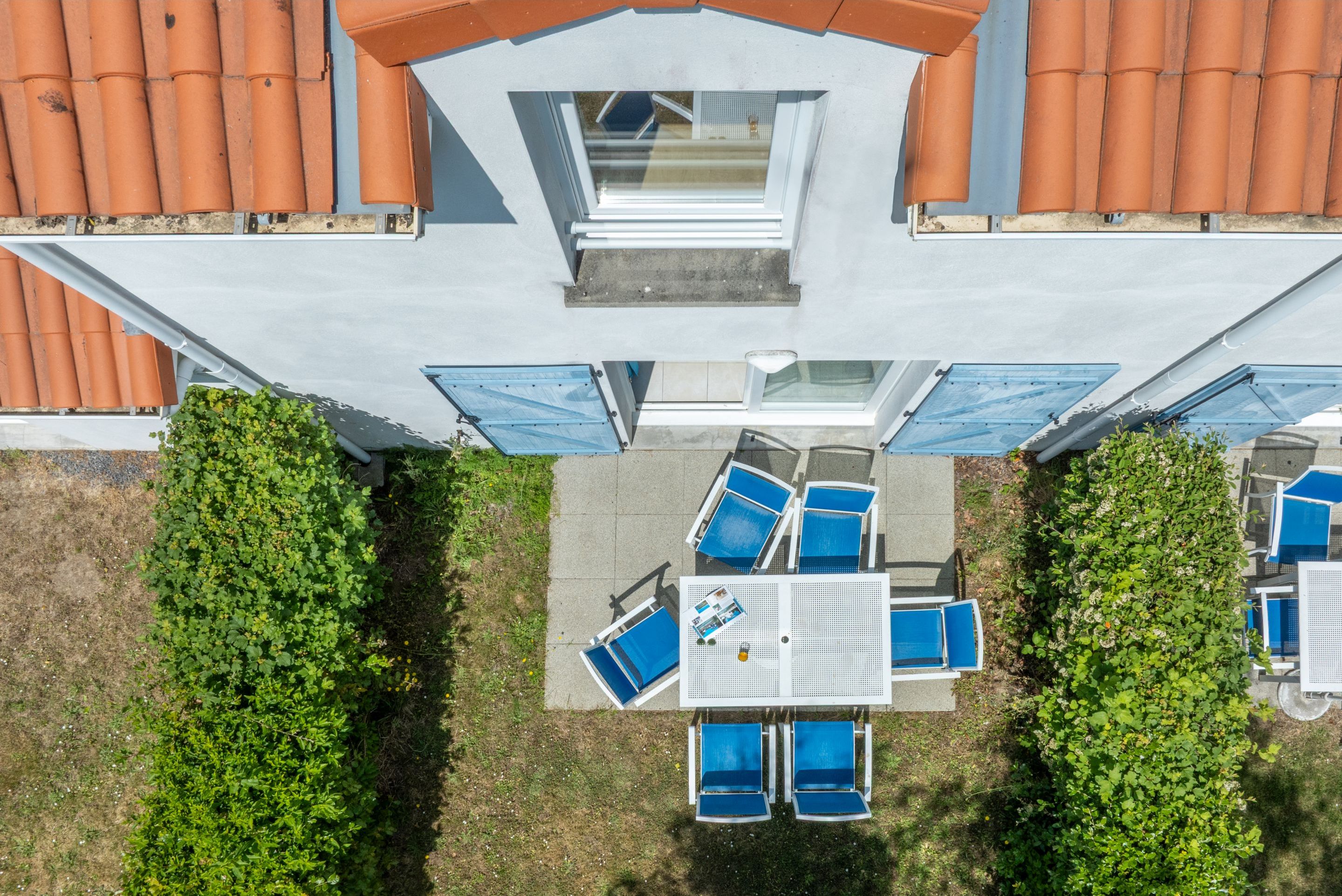 An aerial view of a building with a rooftop terrace, a table with chairs, and a small garden area.