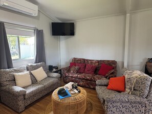 Ein Wohnzimmer mit gemusterten Sofas, einem Flachbildfernseher und einem Korbsessel.