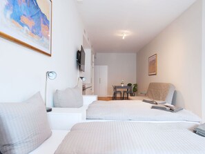 Ein Hotelzimmer mit zwei Betten, einem Schreibtisch, einem Sessel, einem Fernseher und einem Bild an der Wand.