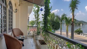 A balcony with wicker chairs, potted plants, and a view of a lake with boats. - Panna Villas Udaipur (Udaipur)