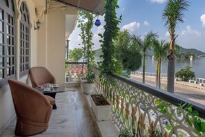 A balcony with wicker chairs, potted plants, and a view of a lake with boats. - Panna Villas Udaipur (Udaipur)