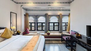 A hotel room with a bed, a desk, a chair, a TV, and a balcony with a view. - Panna Villas Udaipur (Udaipur)