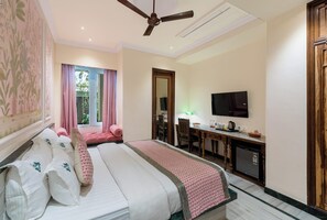 Una camera d'hotel con un letto, una scrivania, una televisione e un ventilatore a soffitto.
