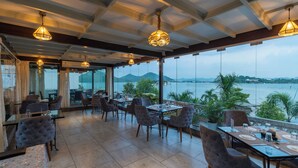 A restaurant with tables and chairs, large windows with a view of the sea, and hanging pendant lights. - Panna Villas Udaipur (Udaipur)