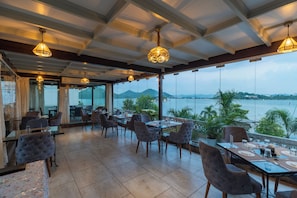 A restaurant with tables and chairs, large windows with a view of the sea, and hanging pendant lights. - Panna Villas Udaipur (Udaipur)