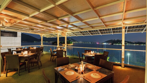 A restaurant with tables set for dining, overlooking a body of water at night. - Panna Villas Udaipur (Udaipur)