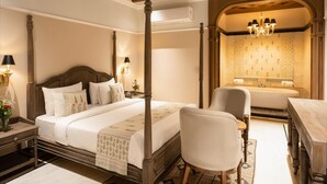 A four-poster bed with a nightstand, a chair, a desk, and a bathroom with a bathtub and a chandelier. - Panna Villas Udaipur (Udaipur)