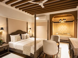 A four-poster bed with a nightstand, a chair, a desk, and a bathroom with a bathtub and a chandelier. - Panna Villas Udaipur (Udaipur)