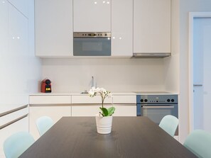 Une cuisine moderne avec des meubles blancs, un four encastré et une horloge numérique.
