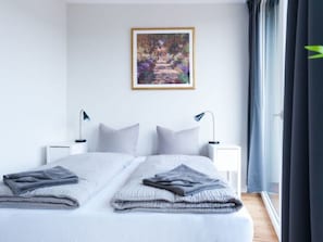 Une chambre d’hôtel moderne avec un grand lit, deux tables de chevet avec des lampes, un tableau encadré au mur et une vue sur l’extérieur.
