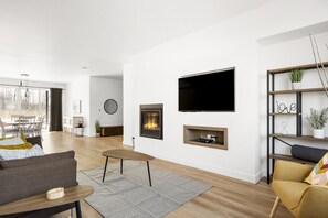 A modern living room with a fireplace, a flat-screen TV, and a bookshelf. - Le Memph Orignal: 3 bedrooms pool hot tub lac Memphrémagog (Magog)