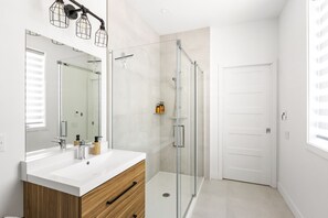 Une salle de bain moderne avec une douche à parois de verre, un meuble-lavabo blanc doté d’un placard en bois et un grand miroir.