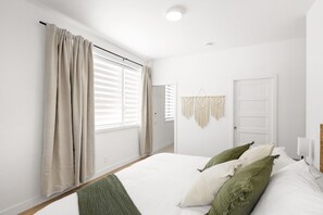 Une chambre à coucher avec un lit, des rideaux, une porte et une décoration en macramé accrochée au mur.