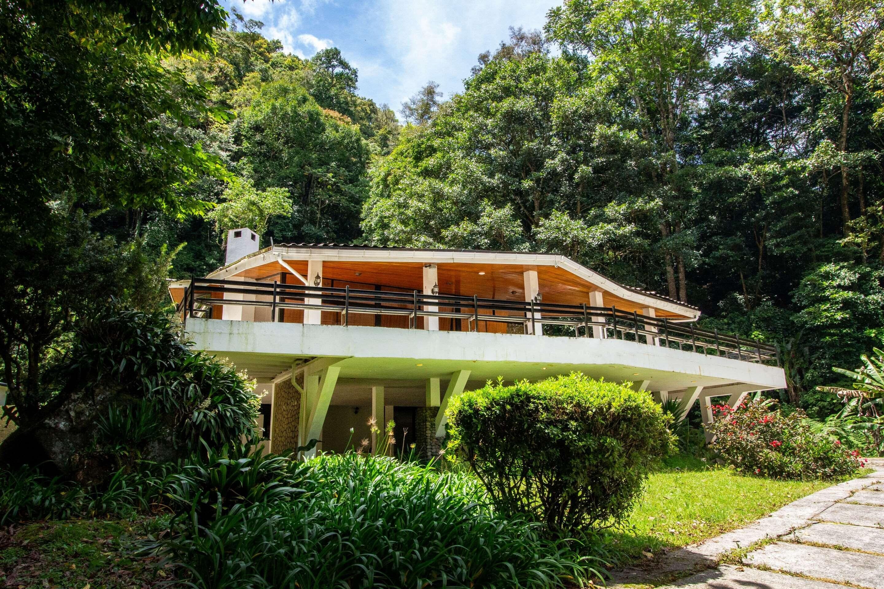 A modern house with a curved roof, surrounded by lush greenery and a stone pathway.
