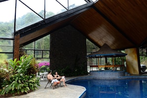 A pool area with a gazebo, stone walls, and large windows overlooking a forested area.