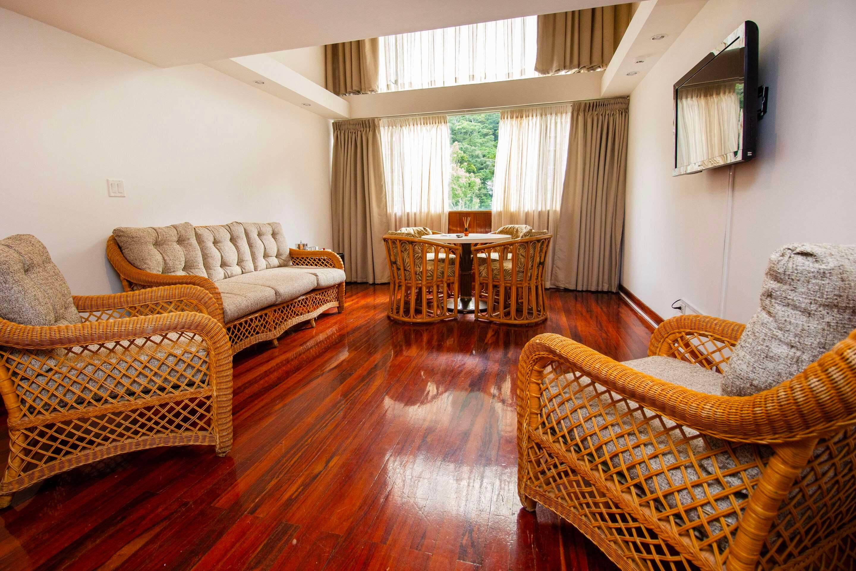 A room with a sofa, two wicker chairs, a small table, and a TV mounted on the wall.