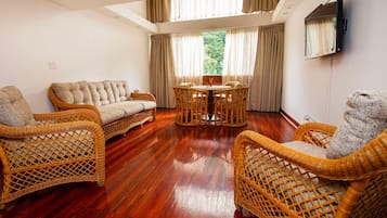 A room with a sofa, two wicker chairs, a small table, and a TV mounted on the wall.
