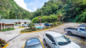A parking lot with cars, a building with a stone facade, and a mountainous backdrop.