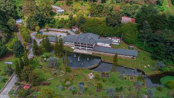 An aerial view of a large building with a central courtyard, surrounded by lush greenery and a small lake.