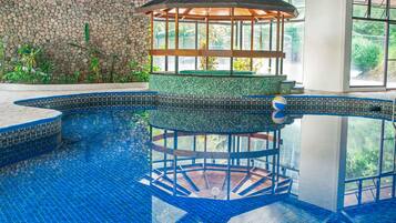 A swimming pool with a circular deck, a gazebo, and a stone wall.