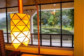 A room with a large window, a hanging light fixture, and a view of a park with a pond.