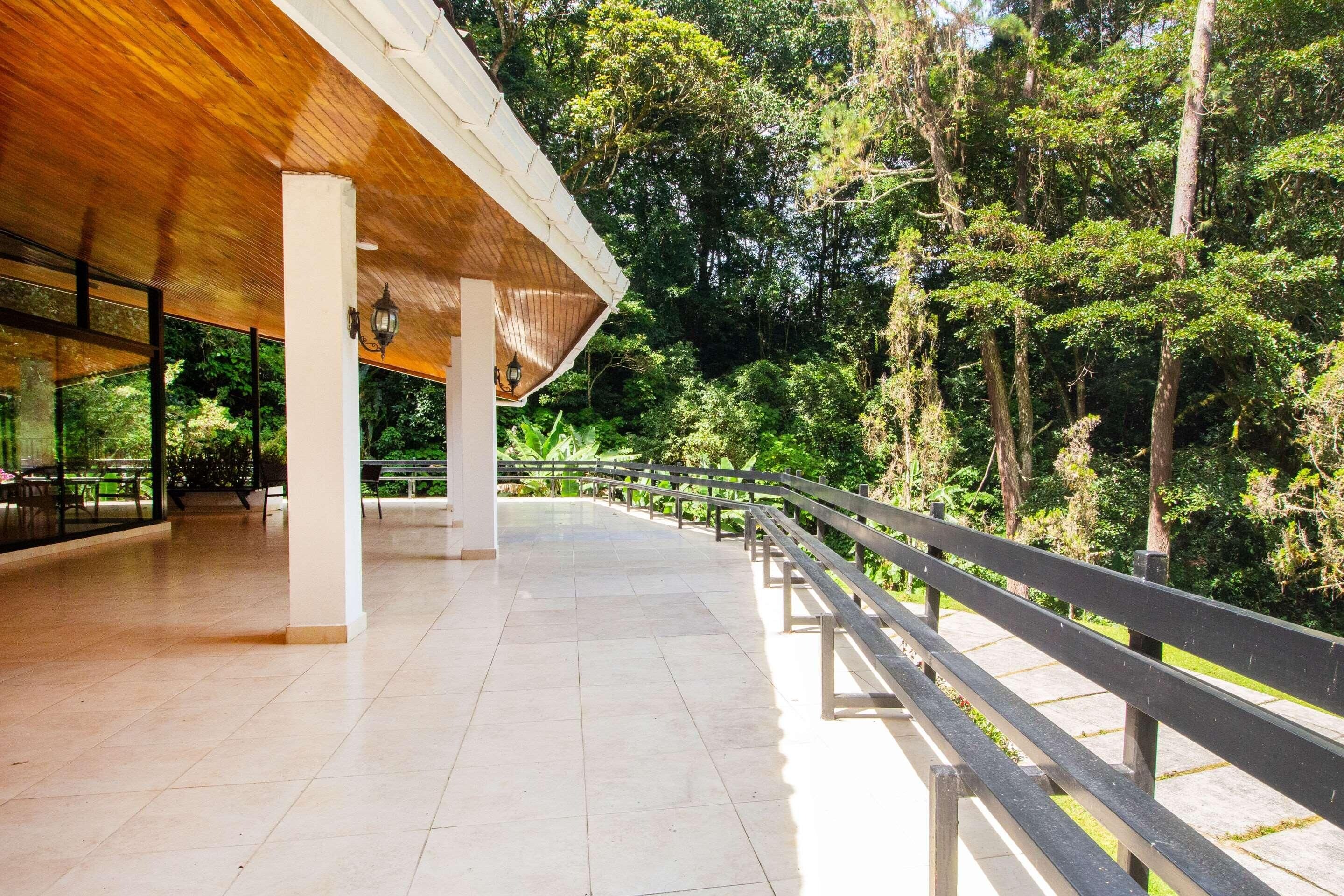 An outdoor covered area with a wooden roof, tiled flooring, and a railing overlooking a forested area.
