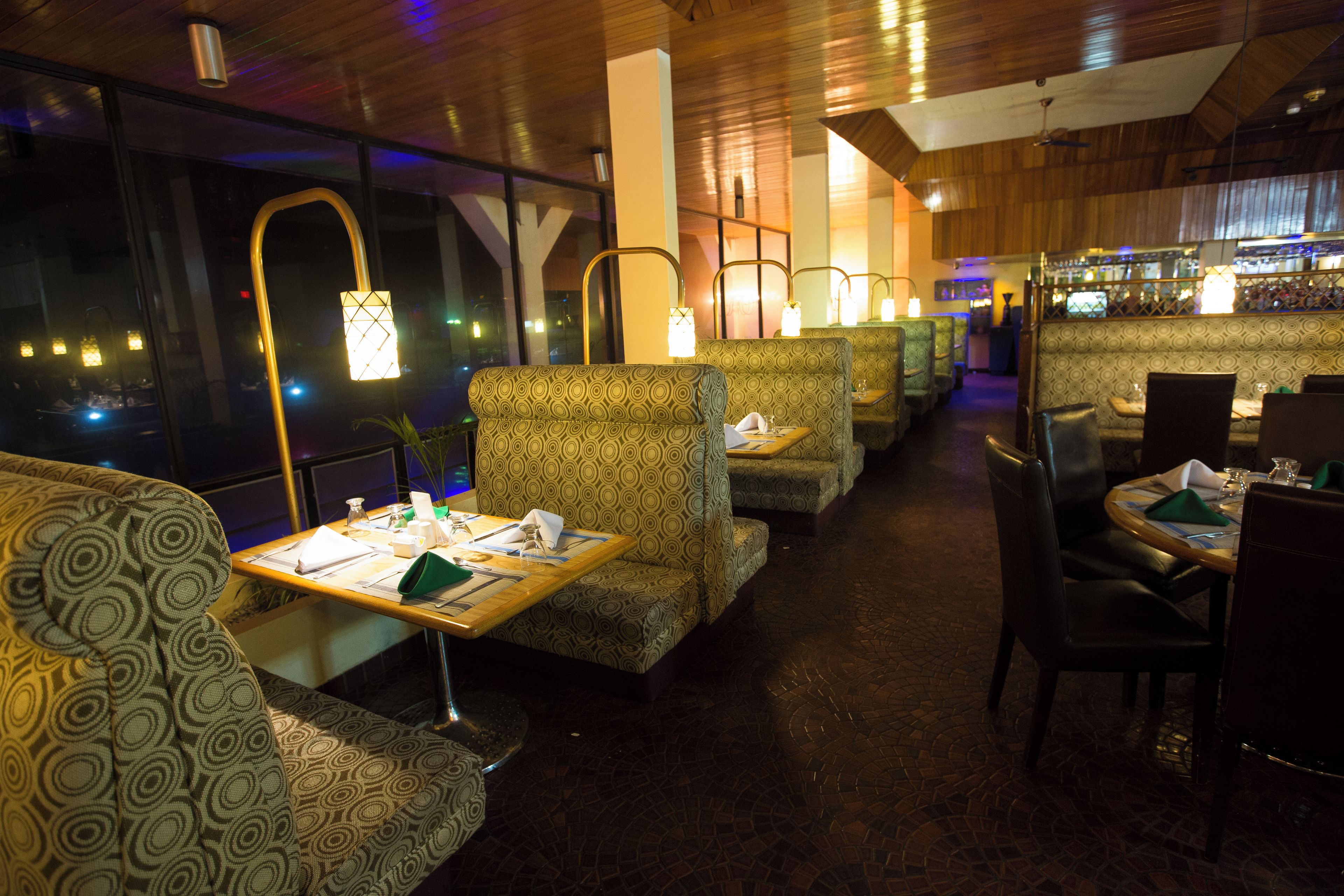 A restaurant with patterned booths, tables with menus, and a bar in the background.