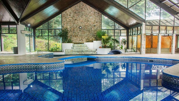 A large indoor swimming pool with a stone wall and glass windows.