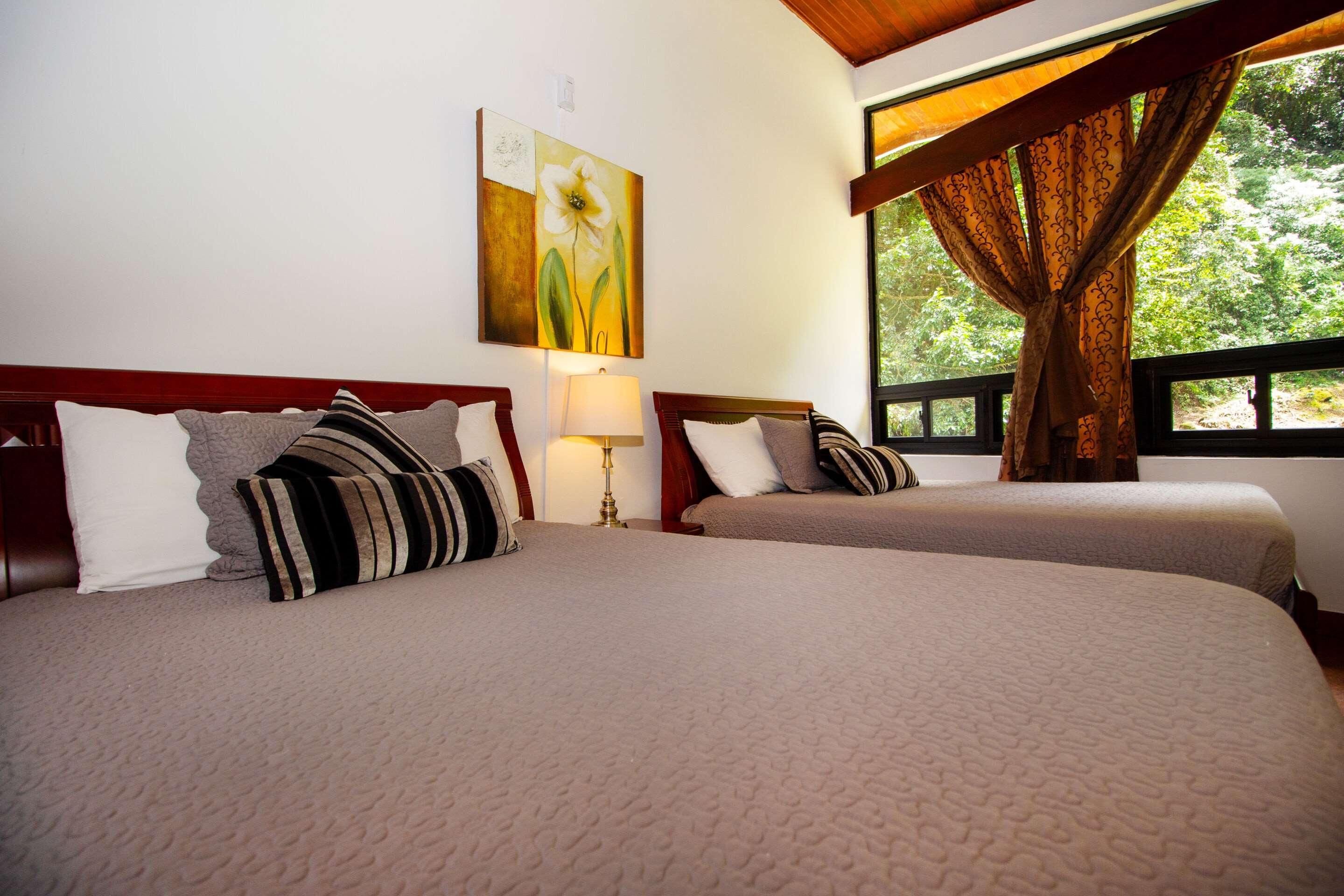 Two beds with headboards, a bedside lamp, a painting, and a window with curtains.