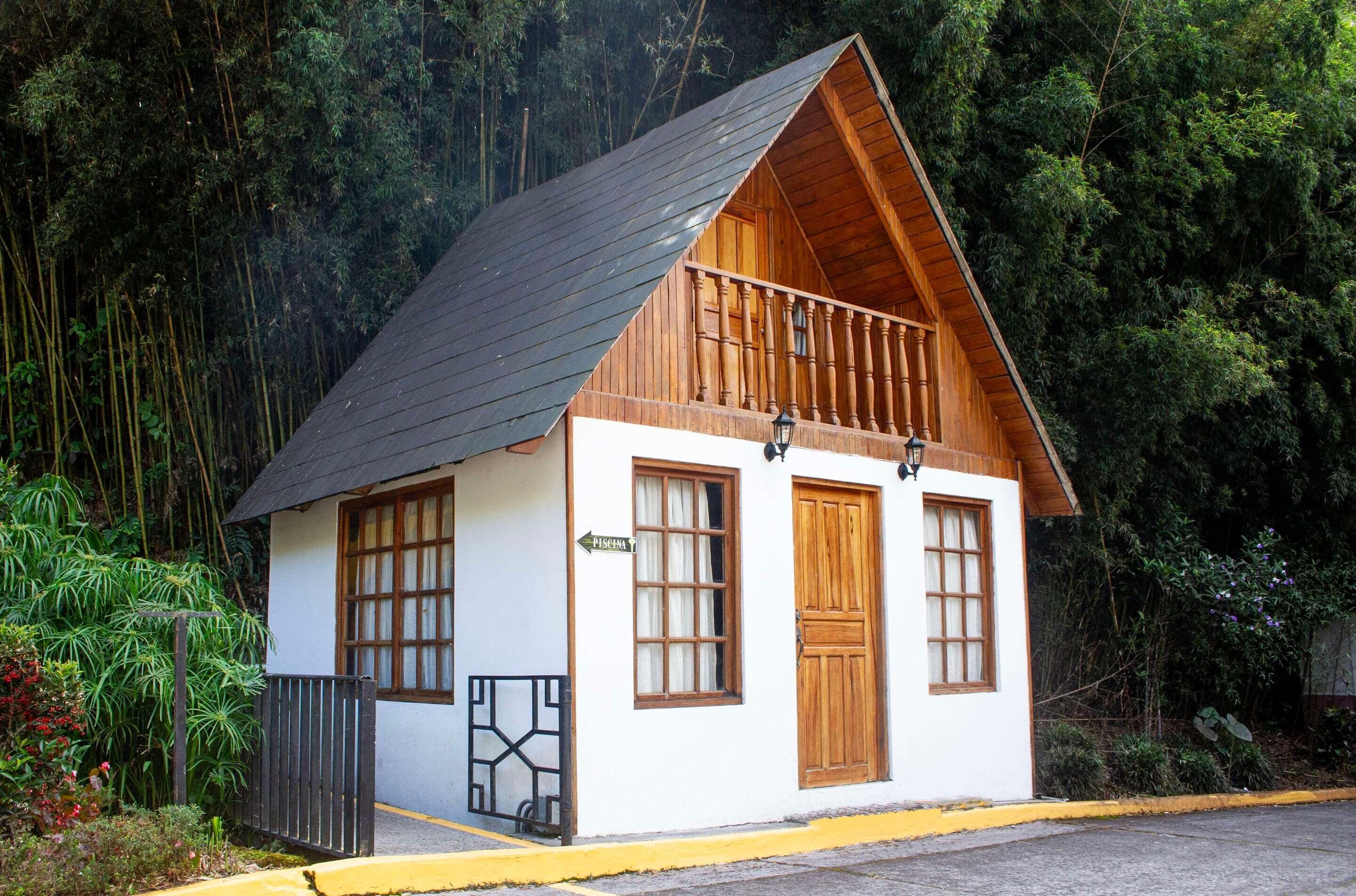 A small, single-story building with a sloped roof, wooden balcony, and a sign indicating 'PISCINA'.