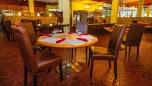 A restaurant with round tables, brown leather chairs, and a tiled floor.