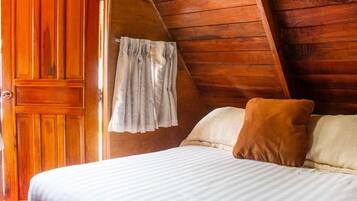 Una habitación de madera con cama, puerta y ventana con cortinas.