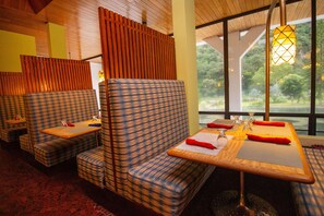 A restaurant with checkered seating, wooden tables, and a view of greenery through large windows.