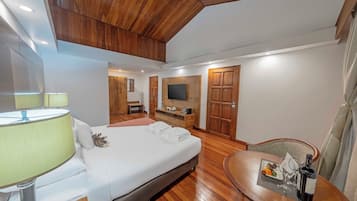 A hotel room with a bed, bedside table, lamp, TV, wooden wardrobe, and a dining area with a table and chairs.