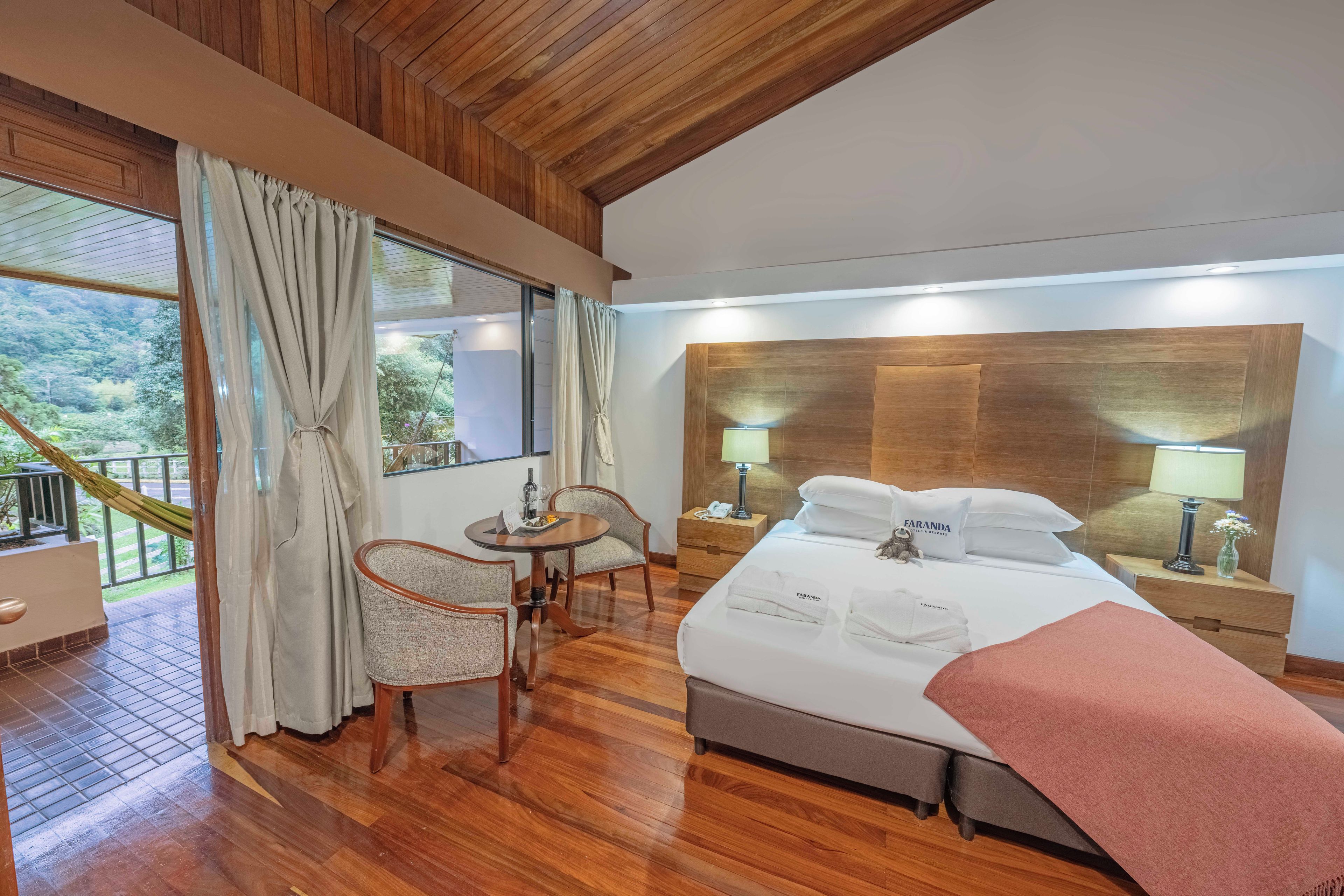 A hotel room with a bed, bedside tables, a desk with a chair, and a view of the outdoors.
