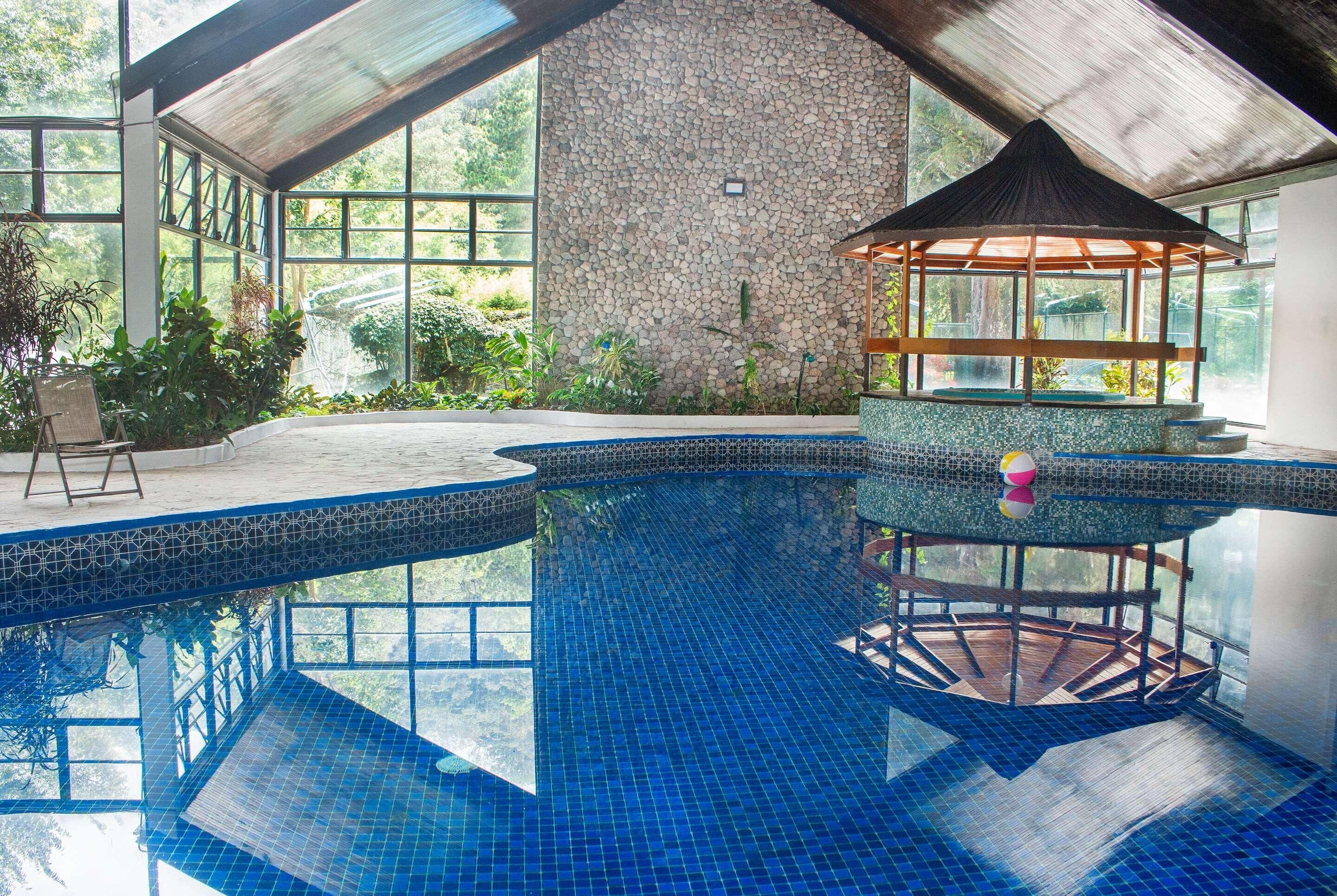 An indoor swimming pool with a stone wall, a gazebo, and a view of greenery outside.