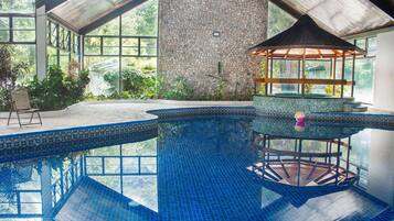 An indoor swimming pool with a stone wall, a gazebo, and a view of greenery outside.