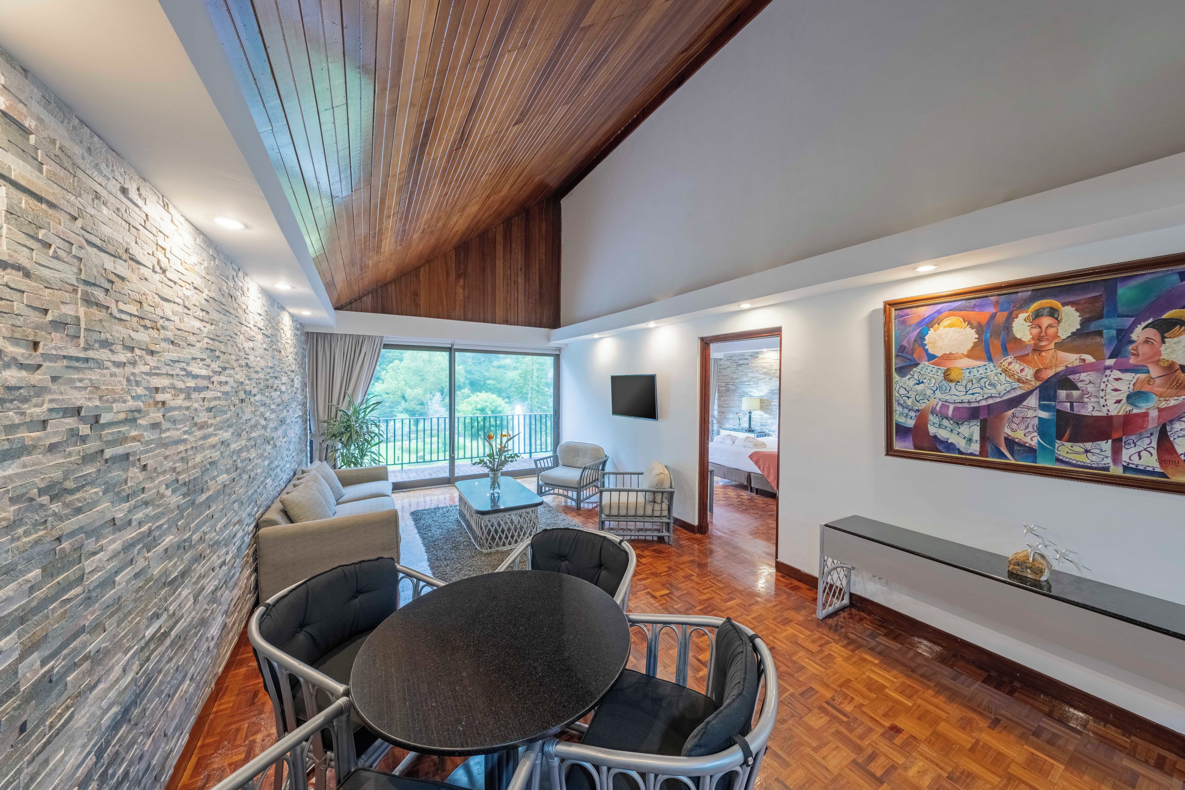 A modern interior with a stone wall, a wooden ceiling, a dining area with a round table, and a large painting.