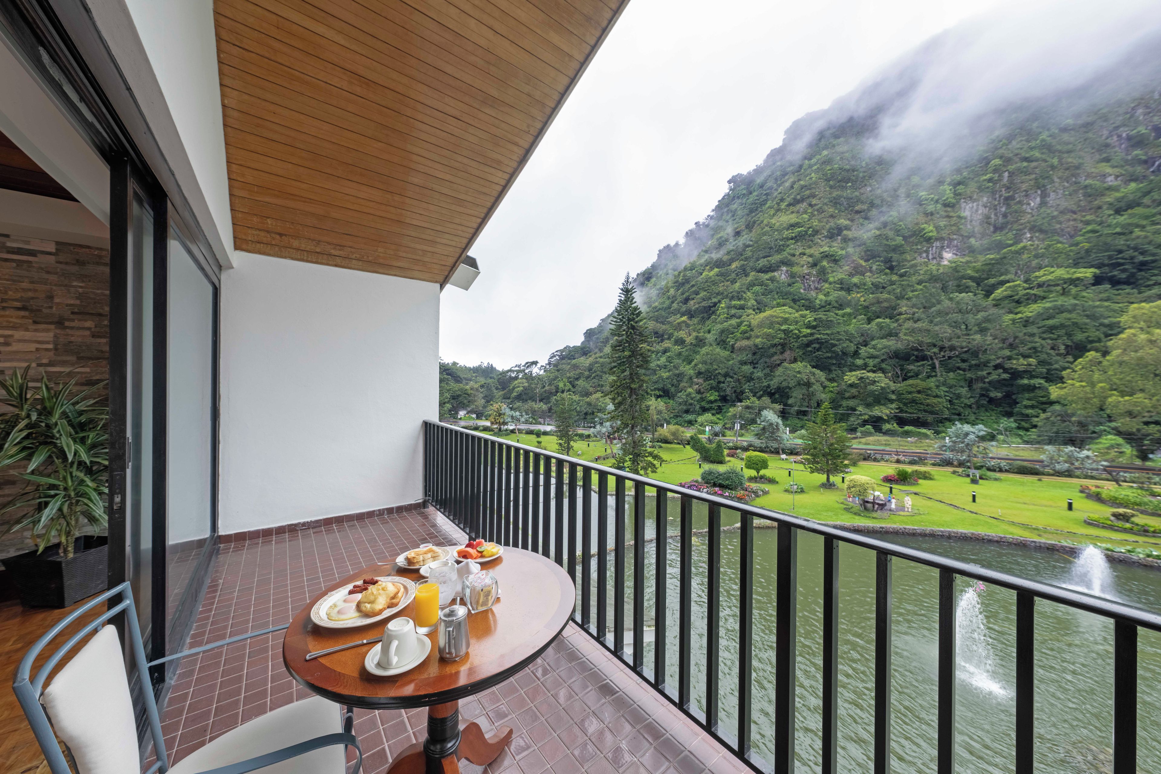 A balcony with a table set for breakfast, overlooking a river and a mountainous landscape.