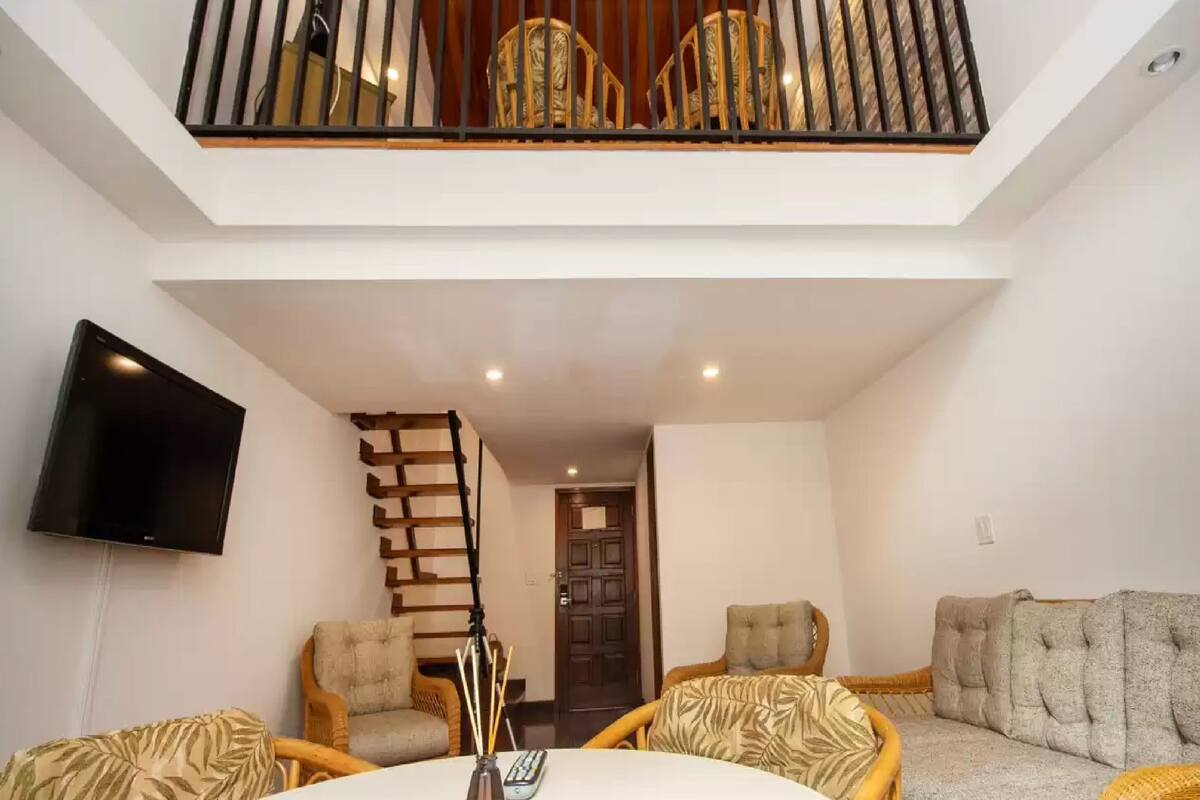 A living room with a TV, wooden furniture, a staircase, and a balcony.