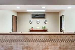A reception area with a tiled counter, a flat-screen TV, three wall clocks, and potted plants. - Econo Lodge Ithaca Area (Ithaca)