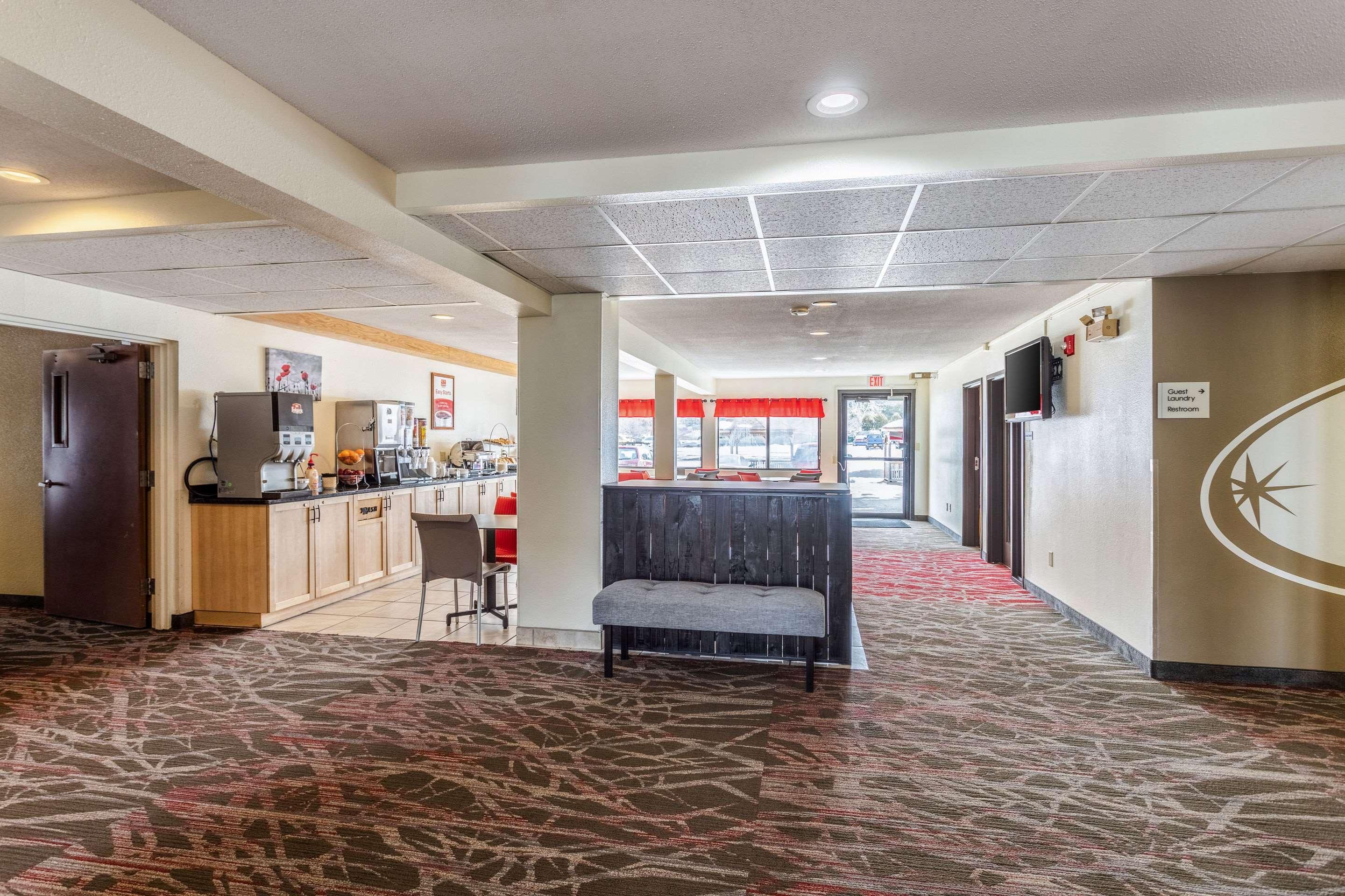 A hotel lobby with a reception desk, a seating area, a kitchenette, and a sign indicating guest amenities.