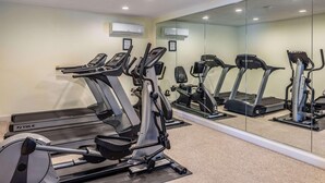 Une salle de sport équipée de plusieurs tapis de course, d’un mur recouvert de miroirs et d’un éclairage au plafond.