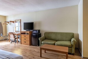 A hotel room with a wooden desk, a television, a green sofa, a wooden coffee table, and a bed. - Econo Lodge Ithaca Area (Ithaca)