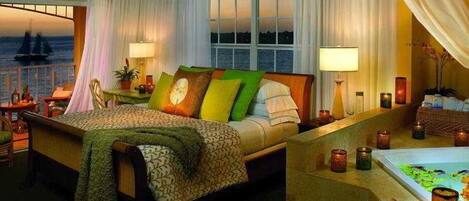 A hotel room with a large bed, a sitting area, a view of the sea, and a balcony with a ship.