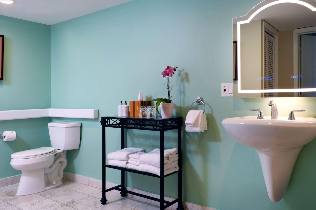 A bathroom with a toilet, sink, and a vanity table with towels and toiletries.