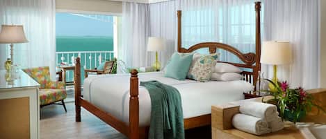 A spacious bedroom with a large bed, a balcony with a view, and a wooden ceiling fan.