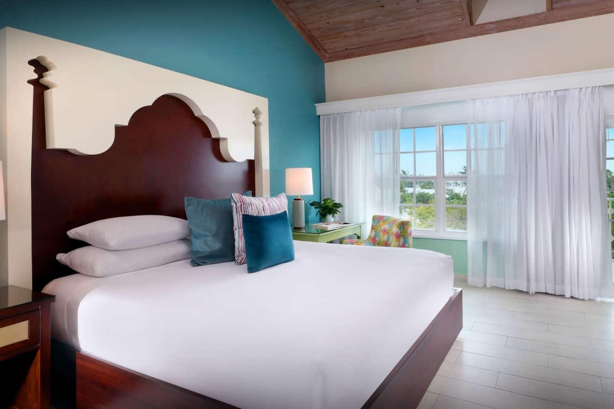 A bedroom with a large bed, a wooden headboard, a nightstand, a lamp, and a window with curtains.