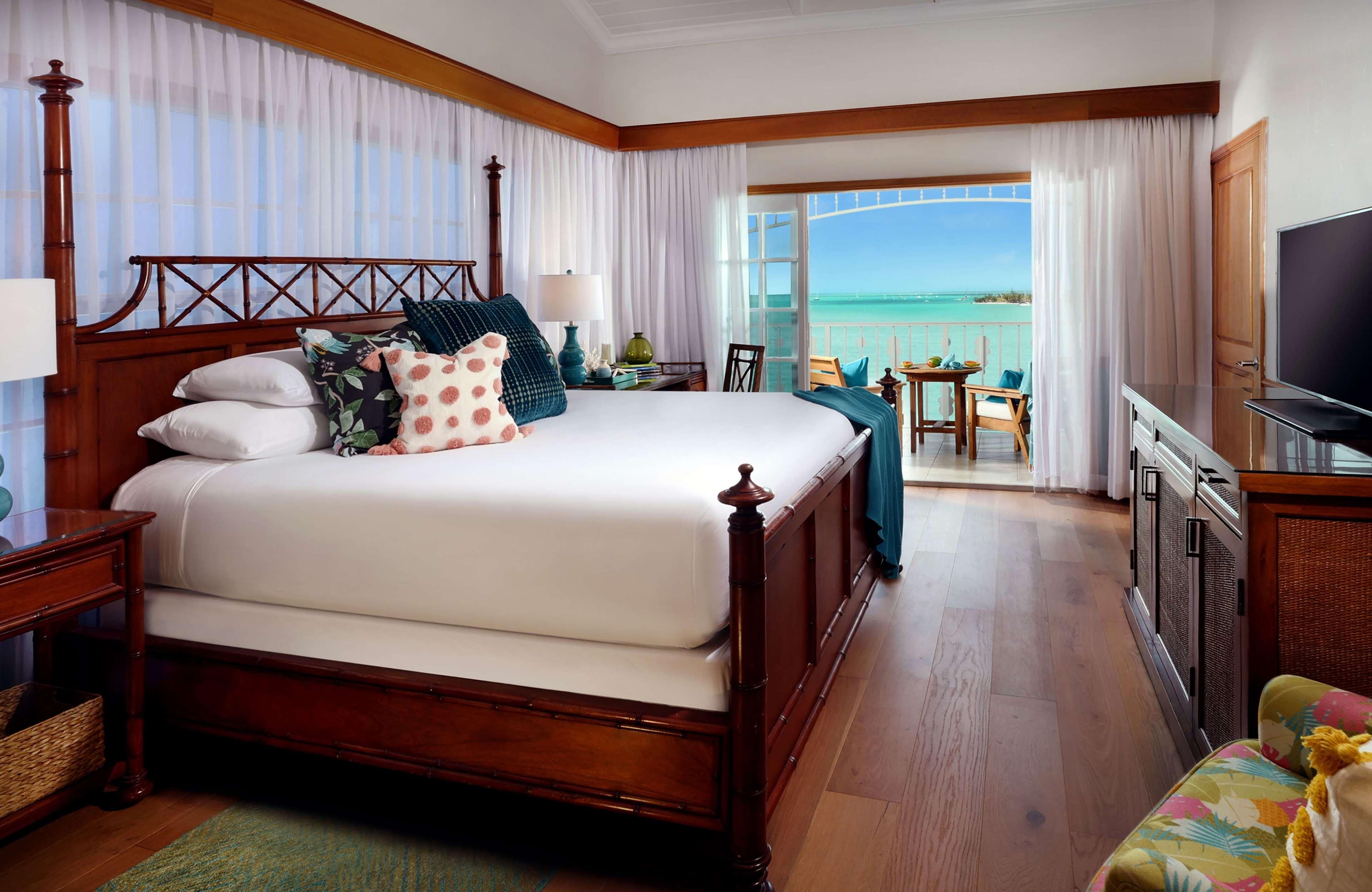 A hotel room with a large bed, a TV, a balcony with a view of the ocean, and a dining area.